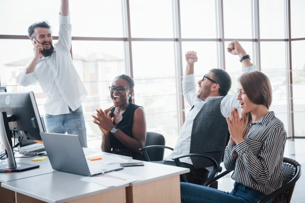 Equipe de escritório celebrando com entusiasmo após uma conquista, simbolizando o sucesso na aprovação de um projeto.