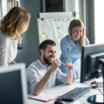 Equipe de trabalho reunida em frente a um computador, sorrindo e discutindo estratégias, representando inovação e aprendizado com IA.