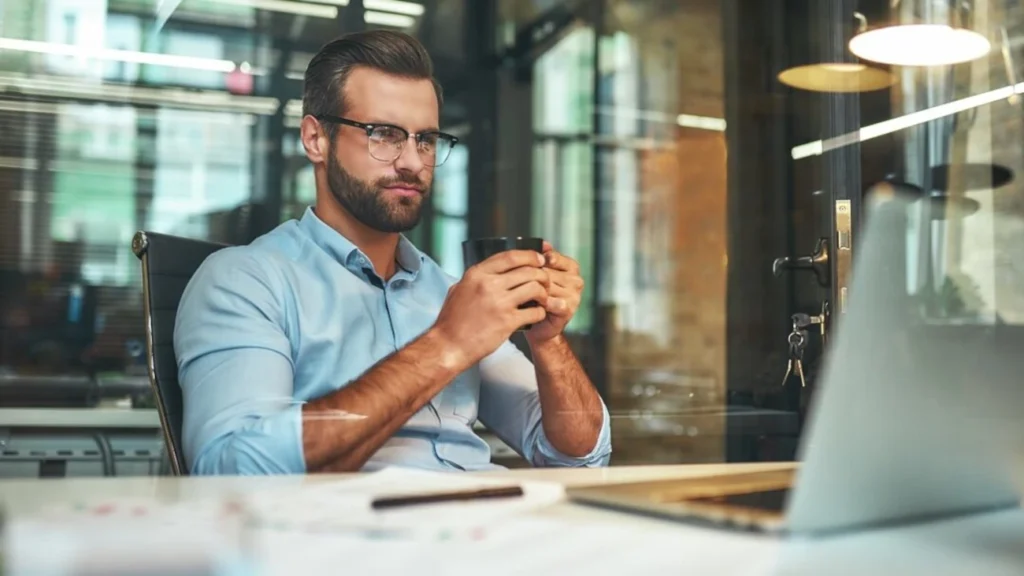 Profissional em um escritório moderno, segurando uma xícara de café enquanto analisa informações no laptop, representando o impacto da IA no desenvolvimento profissional.