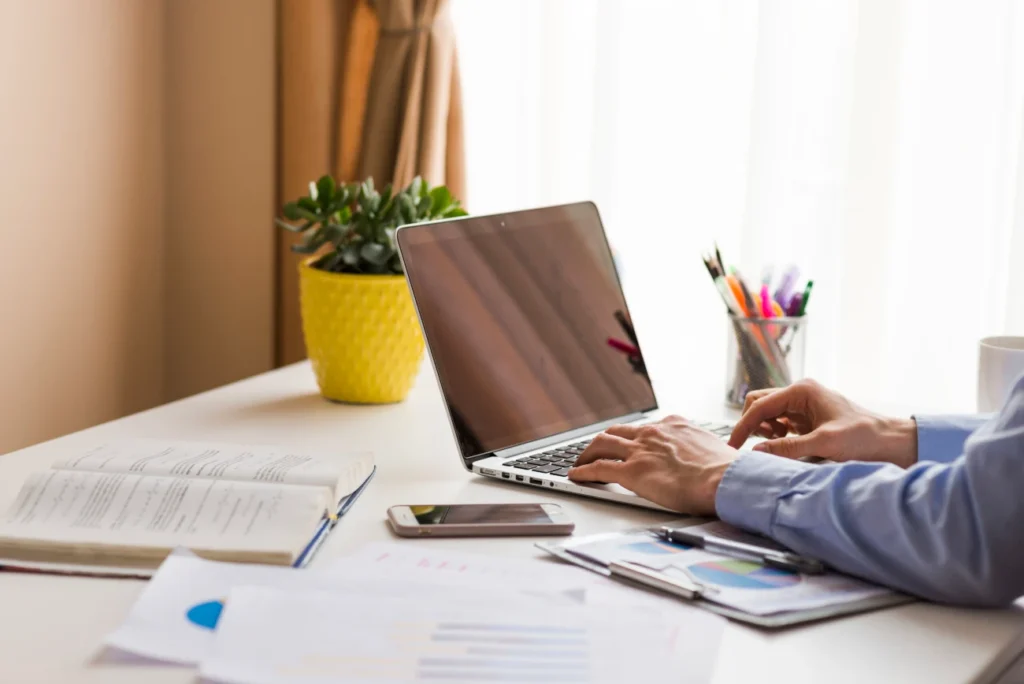 Profissional trabalhando em um laptop em um ambiente organizado, com materiais de estudo e gráficos financeiros, representando aprendizado digital.