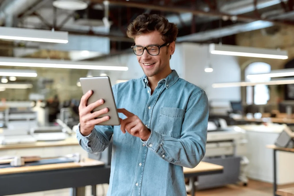 Homem sorridente usando um tablet em um ambiente de trabalho moderno, simbolizando aprendizado digital e treinamento de produto.