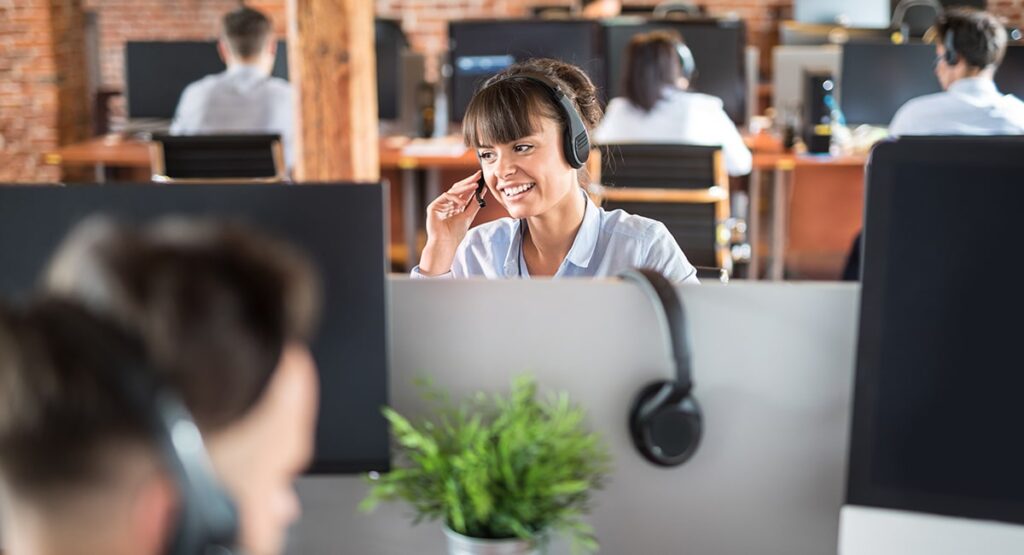 Atendente de suporte ao cliente com headset sorrindo em um ambiente moderno de call center.