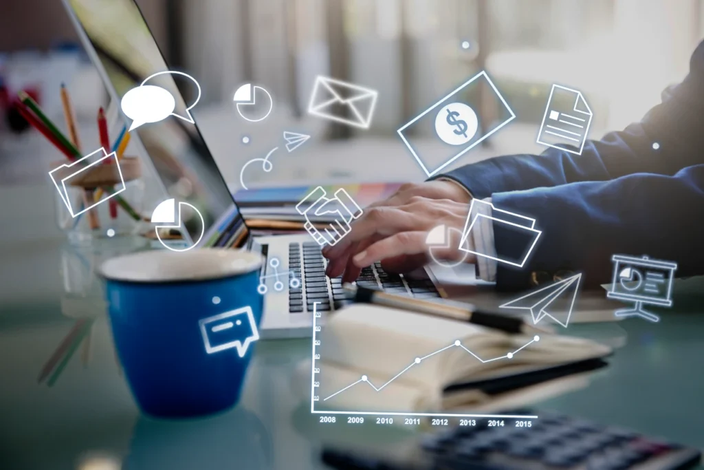 Profissional digitando em laptop com ícones digitais de comunicação, finanças e gráficos, representando plataformas LMS modernas.