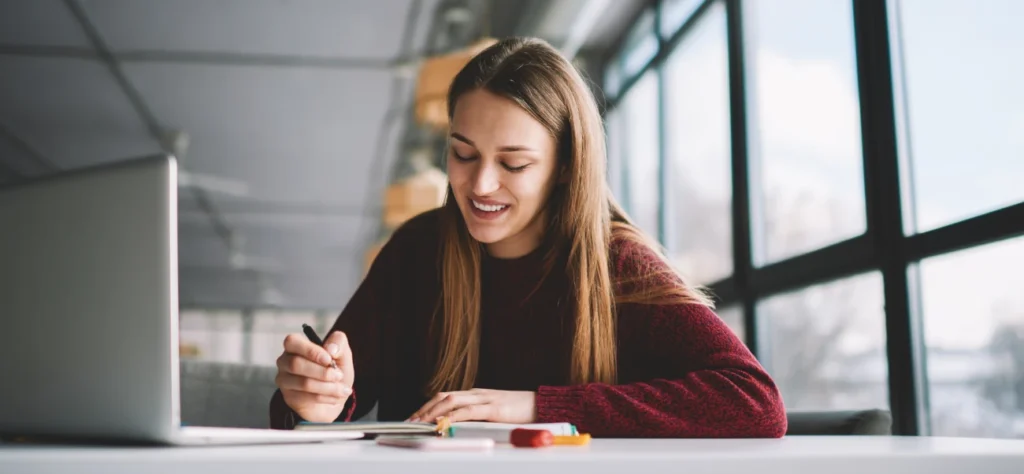 Mulher sorridente estudando em frente ao laptop, representando o uso acessível do TalentLMS para treinamento corporativo na América Latina.