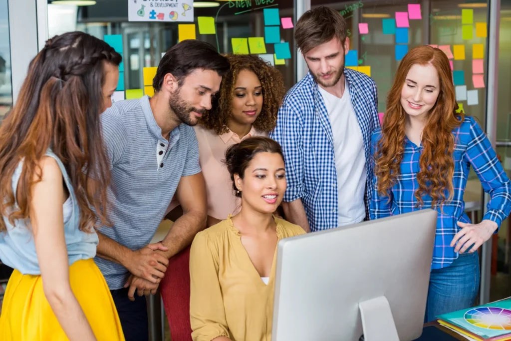 Equipe de profissionais colaborando diante de um computador em ambiente moderno, representando a experiência aprimorada e colaborativa da nova interface do TalentLMS.