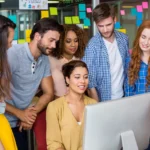 Equipe de profissionais colaborando diante de um computador em ambiente moderno, representando a experiência aprimorada e colaborativa da nova interface do TalentLMS.