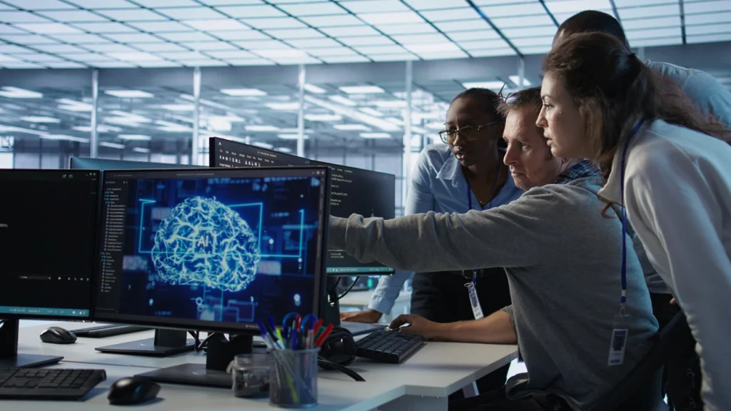 Equipe analisando gráficos de inteligência artificial em monitores, representando o desenvolvimento de habilidades em IA no ambiente corporativo.