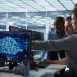 Equipe analisando gráficos de inteligência artificial em monitores, representando o desenvolvimento de habilidades em IA no ambiente corporativo.