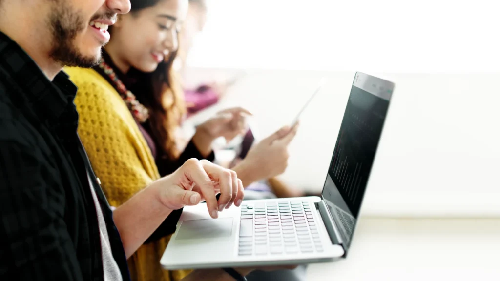 Grupo de pessoas utilizando laptops e tablets em ambiente colaborativo, com foco em tecnologia e aprendizado online.