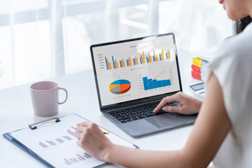 Profissional analisando gráficos de desempenho e métricas de treinamento em um laptop, com relatórios impressos sobre a mesa.