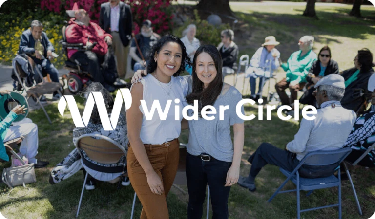 Grupo reunido ao ar livre em uma atividade de integração comunitária, com destaque para o logotipo “Wider Circle” sobreposto à imagem.